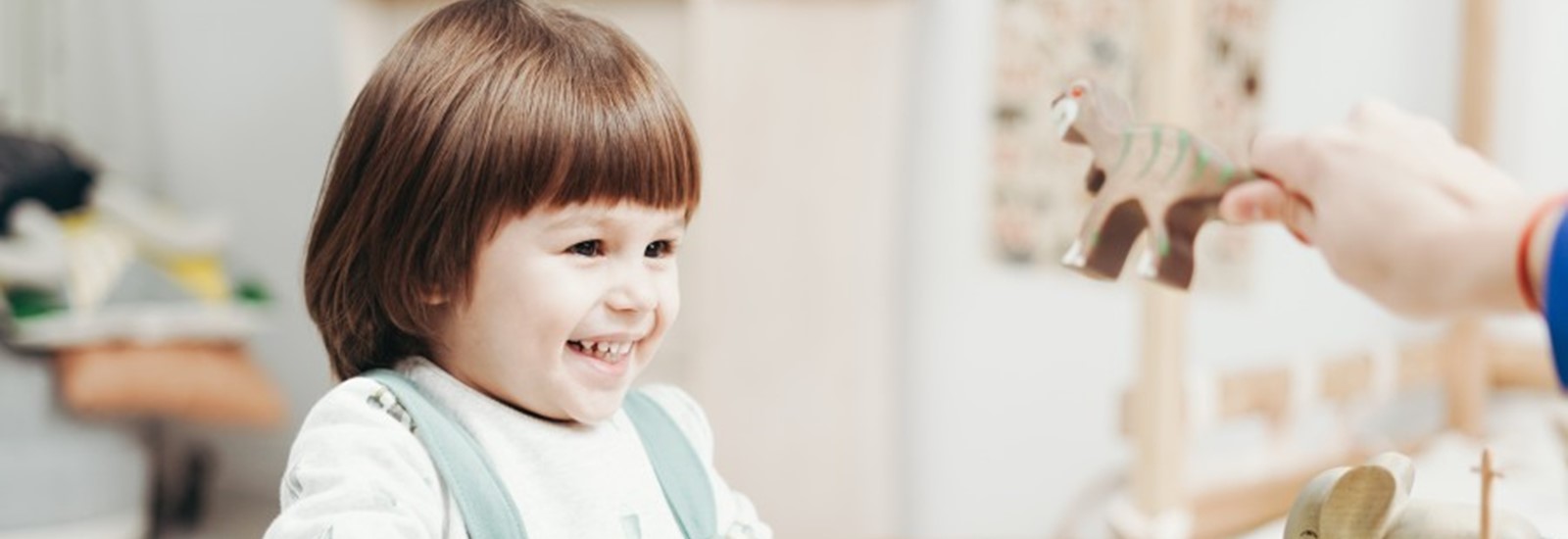 Klein meisje met bruin haar lachend aan het spelen met speelgoed in de crèche