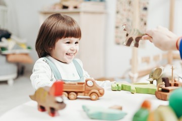 Klein meisje met bruin haar lachend aan het spelen met speelgoed in de crèche